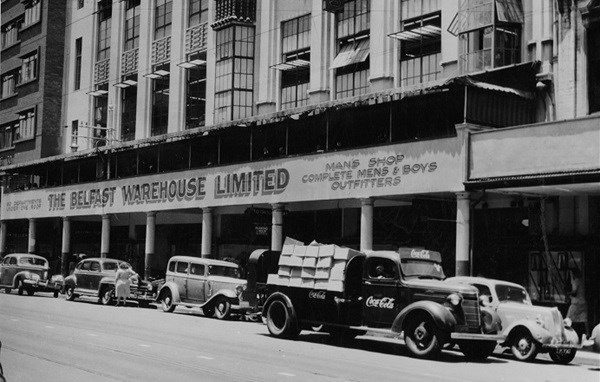 Coca-Cola delivery truck filled with boxes in South Africa. The Belfast warehouse limited building in background. (1940)