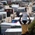 A woman carries a bucket of fresh water to an informal settlement in Khayelitsha, near Cape Town. South Africa has the widest wealth gap in the world. Photo by RODGER BOSCH/AFP via Getty Images