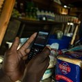 A man makes a payment from his mobile phone for basic food items including bread at a local tuck shop in Epworth, on the outskirts of Harare. Photo by Jekesai Njikizana/AFP via Getty Images