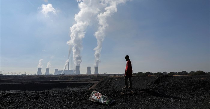 A child collecting chunks of coal looks on at a colliery while smoke rises from the Duvha coal-based power station owned by state power utility Eskom, in Emalahleni. SOurce: Reuters/Siphiwe Sibeko