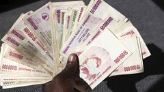A man poses with a handful of Zimbabwean dollars at a bank in central Harare, 15 June 2015. Zimbabweans began exchanging old notes of local dollars for US dollars, as President Robert Mugabe's government seeks to officially bury the worthless currency. Reuters/Philimon Bulawayo/File Photo