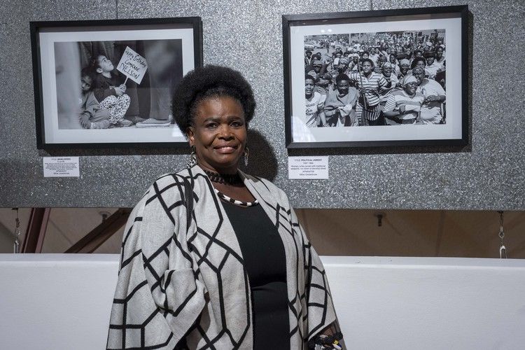 Belinda Hlaka stands next to a photograph taken by Ken Oosterbroek where she appears with a group of women staging a protest against political violence in the township of Kagiso in the 1990s.
