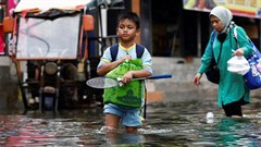 People walk through water at a flooded area affected by rising sea levels and land subsidence in North Jakarta, Indonesia, 20 November 2024. Reuters/Willy Kurniawan/File Photo