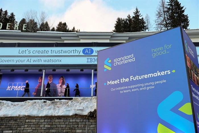 People walk next to a Standard Chartered banner, on the first day of the annual meeting in Davos, Switzerland, 15 January 2024. Reuters/Denis Balibouse/File Photo